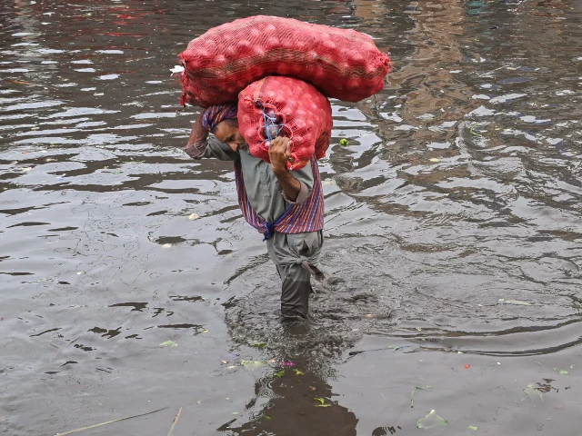 a laborer carries sacks of onions while wading through a flooded street after heavy monsoon rains in lahore on july 16 2025 photo afp